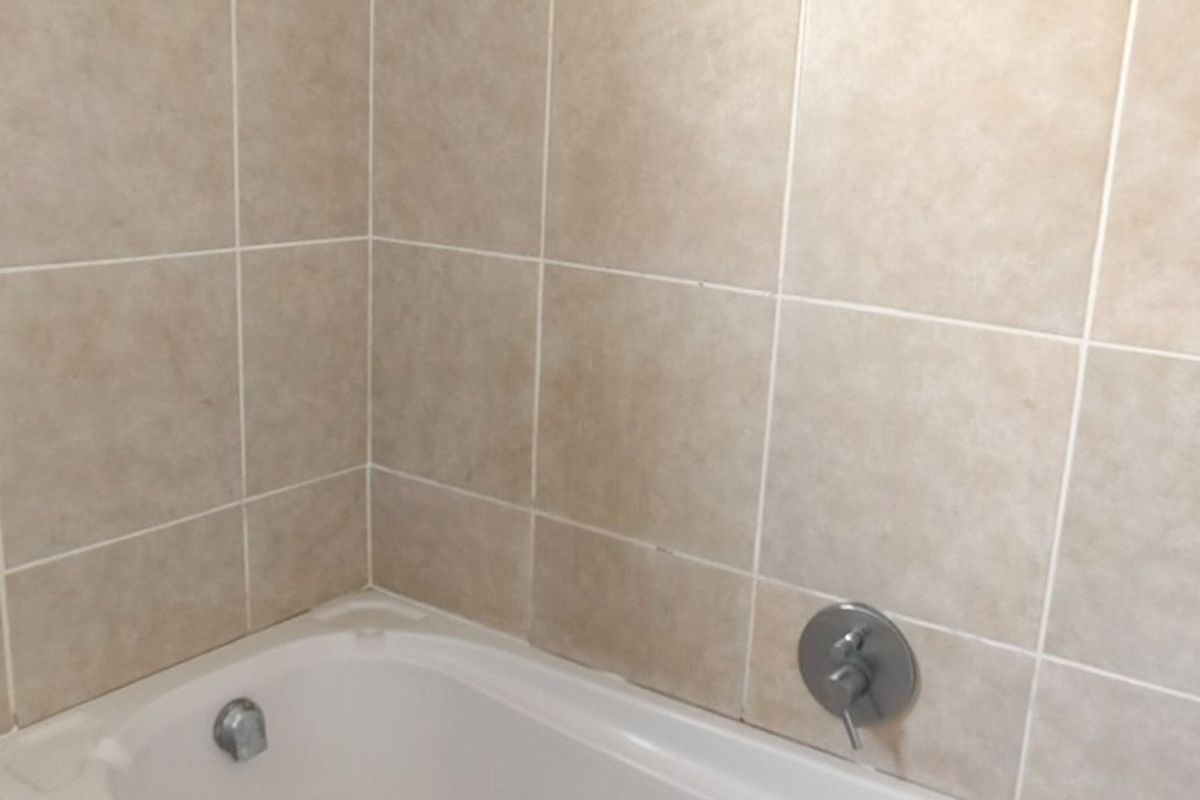 A functional bathroom featuring a built-in bathtub with a shower head and neutral wall tiling.
