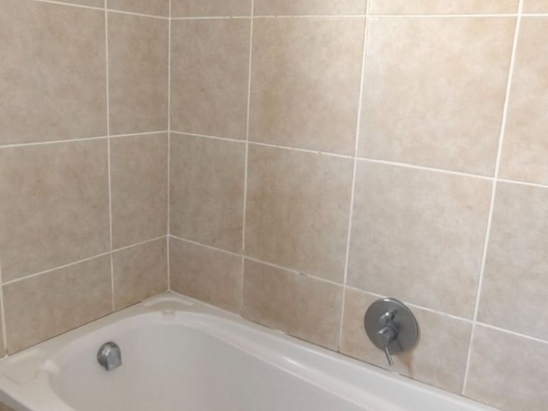 A functional bathroom featuring a built-in bathtub with a shower head and neutral wall tiling.