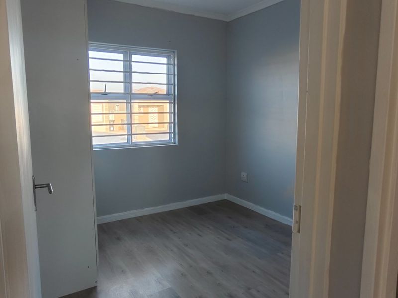 A clean, empty bedroom featuring modern laminate flooring, neutral grey walls, and a window fitted with security bars.