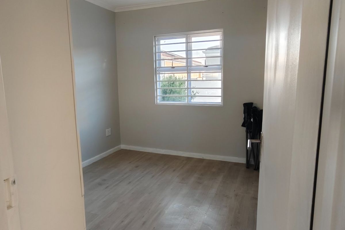A bright, empty bedroom featuring neutral wall tones, modern laminate flooring, and a window fitted with security bars.