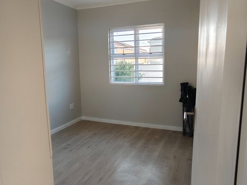 A bright, empty bedroom featuring neutral wall tones, modern laminate flooring, and a window fitted with security bars.