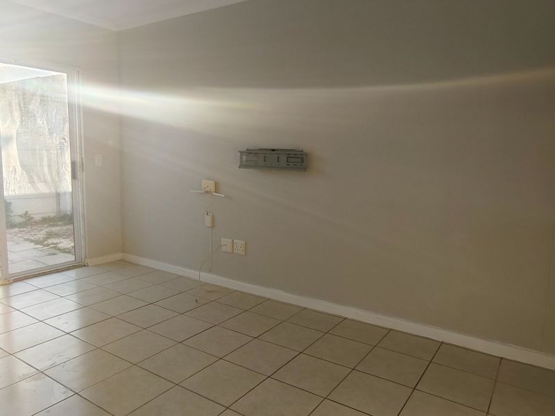An empty open-plan living area featuring tiled flooring and a sliding glass door with security gate, providing access to the exterior.