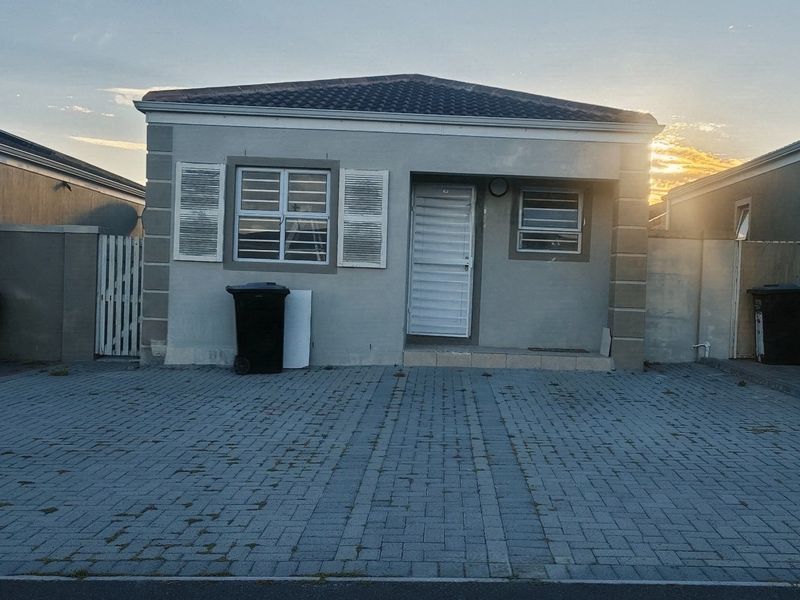 Front elevation of a single-story house featuring a paved driveway, security shutters, and a tiled roof.