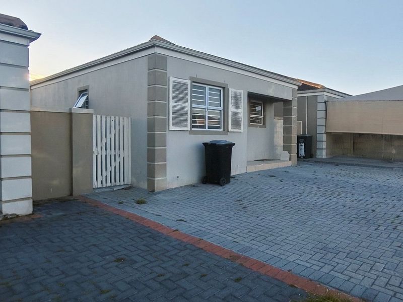 Front exterior view of a single-story house featuring a paved driveway, security shutters on windows, and a gated side entrance.