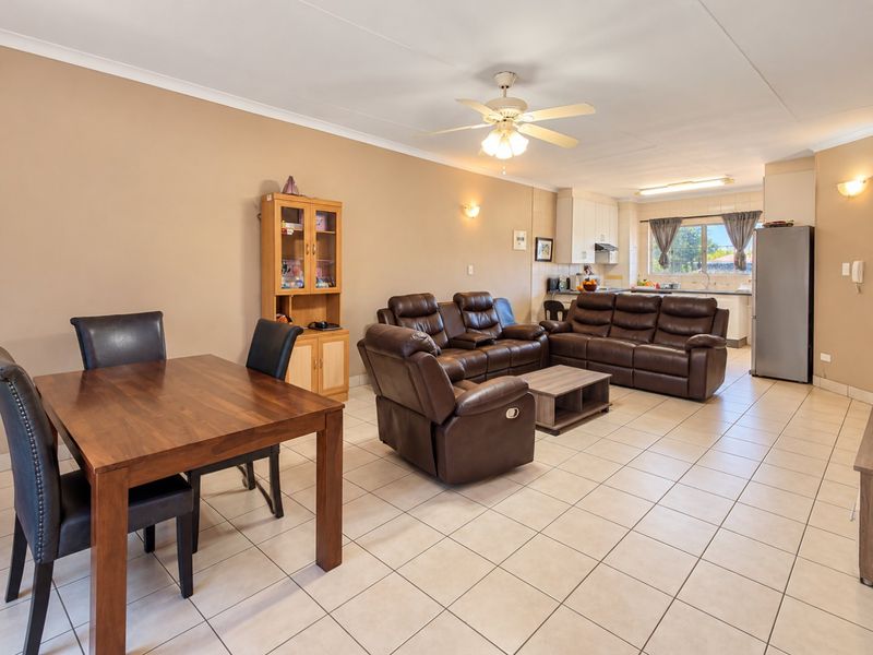 Spacious open-plan living and dining area featuring tiled flooring, a ceiling fan, and an integrated kitchen with functional cabinetry.