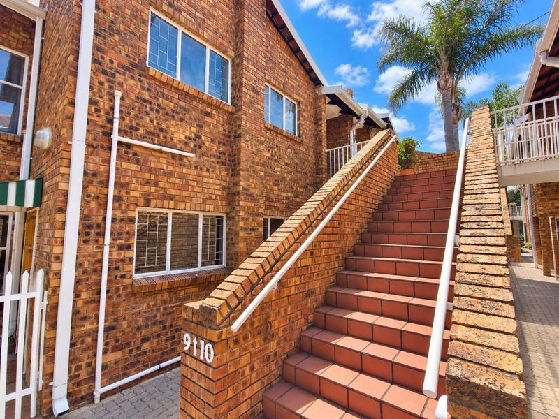 Exterior view of a face brick apartment building featuring a tiled staircase with metal handrails and a paved walkway entrance.
