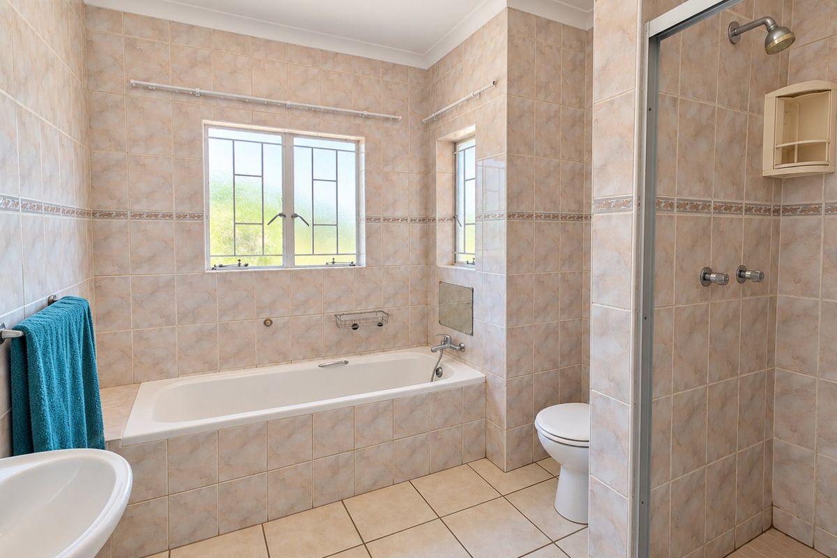 A functional bathroom featuring a built-in bathtub, separate shower enclosure, toilet, and pedestal basin, finished with neutral ceramic wall and floor tiling.