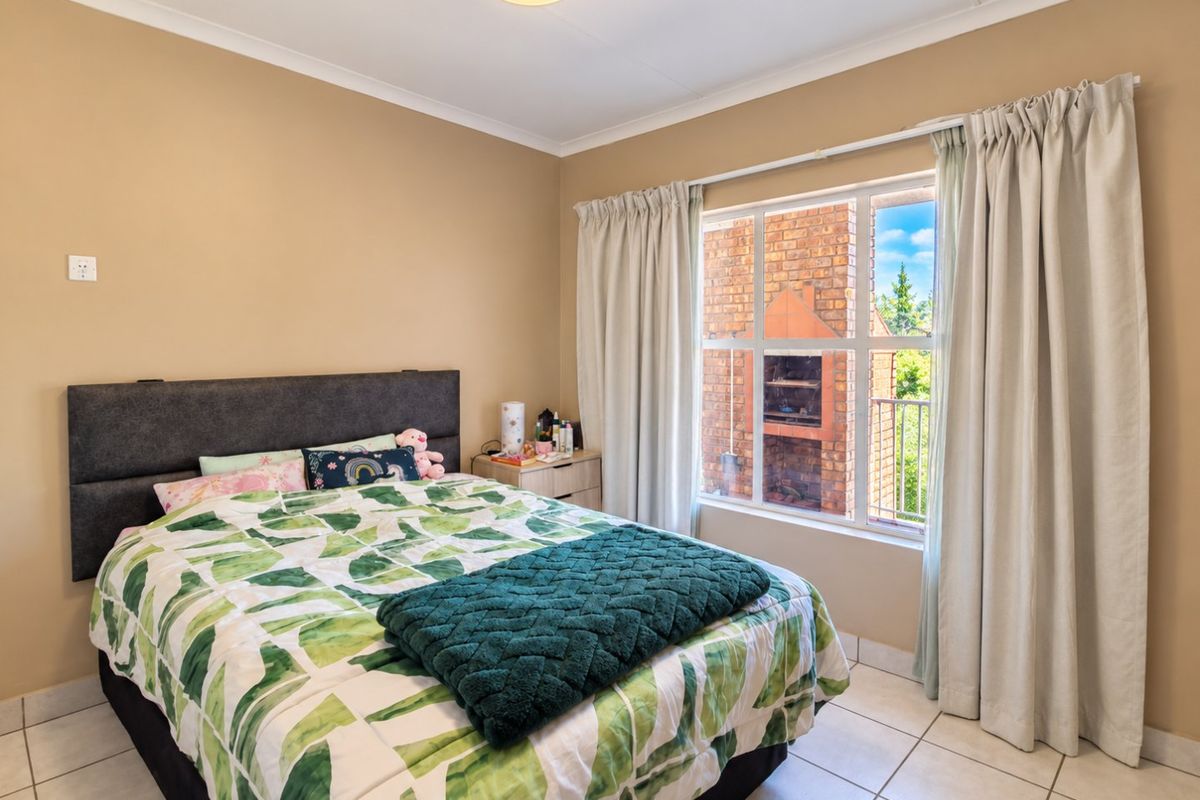 A well-lit bedroom featuring neutral wall tones, tiled flooring, and a large window with views of the exterior brickwork and balcony area.