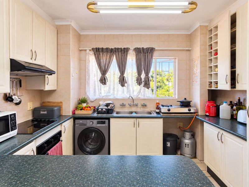 A functional kitchen featuring ample built-in cabinetry, laminate countertops, a double basin sink, and integrated cooking appliances with tiled splashbacks.