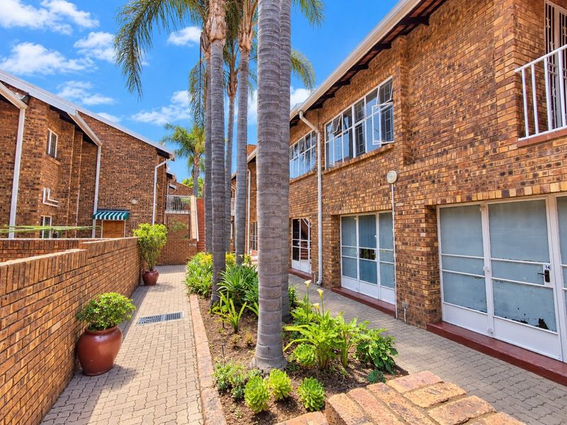 A well-maintained exterior courtyard featuring face brick apartment facades, paved walkways, and established garden beds with mature palm trees.