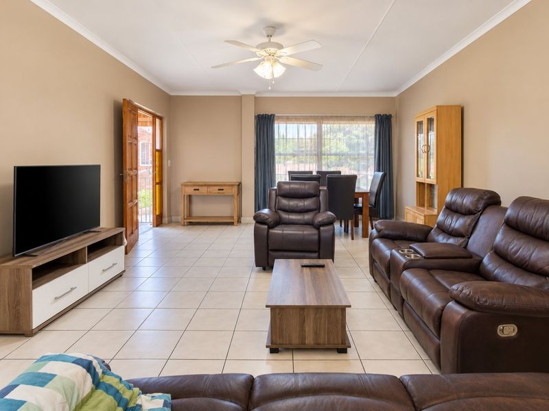 Spacious open-plan living and dining area featuring neutral wall tones, tiled flooring, and a ceiling fan, with direct access to an outdoor balcony.