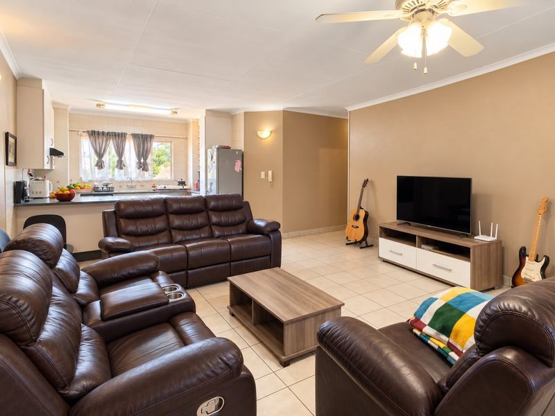 Open plan living area featuring tiled floors, a ceiling fan, and an adjoining kitchen with breakfast counter and cabinetry.