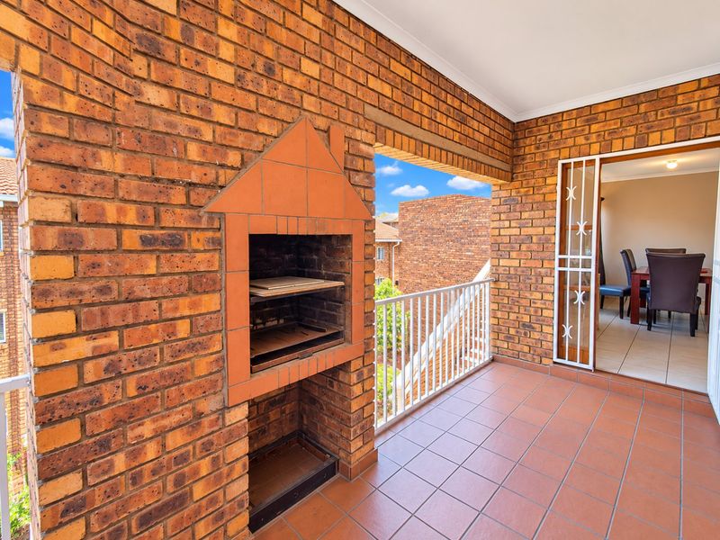 Covered balcony featuring a built-in brick braai, tiled flooring, and a metal balustrade, offering an ideal space for outdoor entertaining.