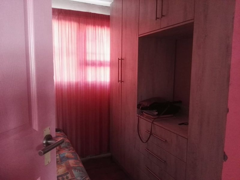 A bedroom featuring built-in wooden wardrobes and laminate flooring, illuminated by natural light through a window with pink curtains.