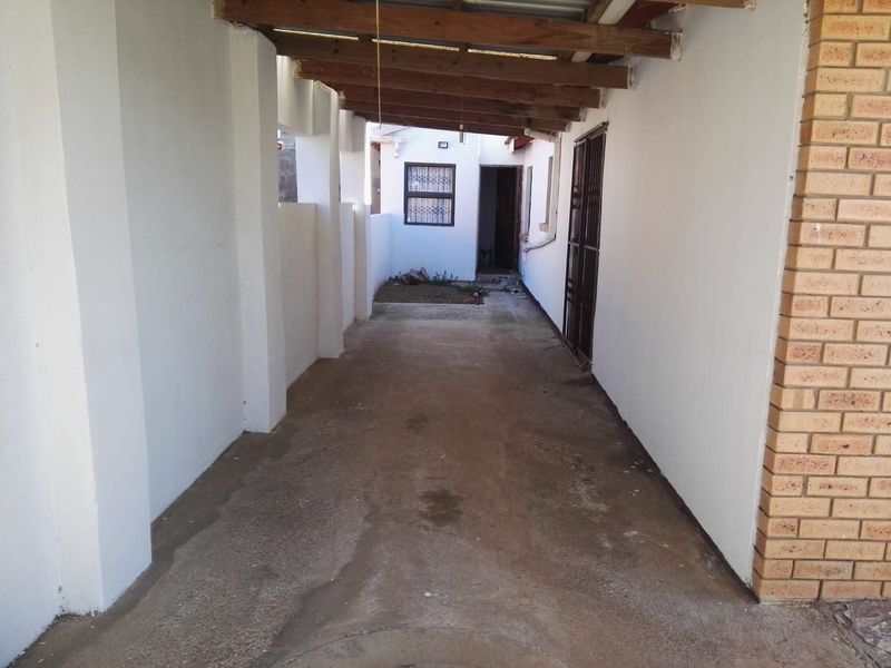 A covered outdoor carport or garage area featuring concrete flooring, exposed timber beams, and secure access points to the main dwelling.