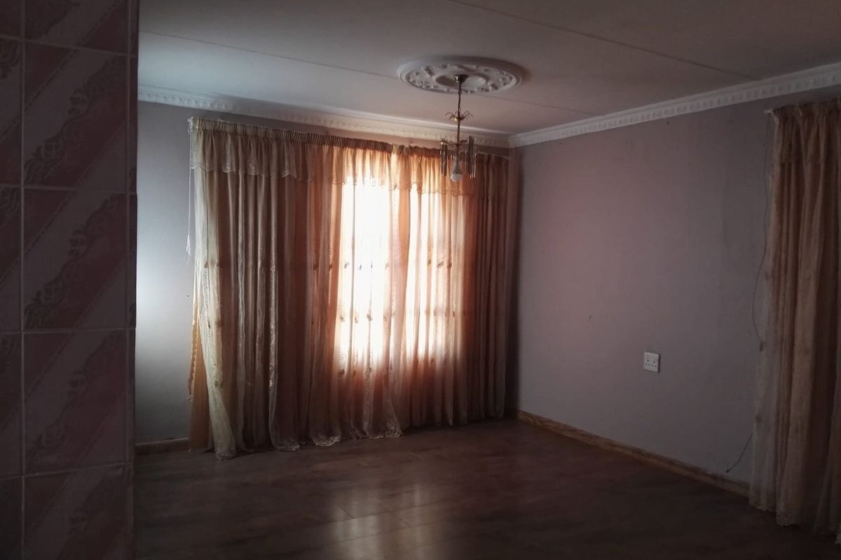 An empty living room featuring laminate flooring, decorative ceiling rose, and coving, providing a blank canvas for interior design.