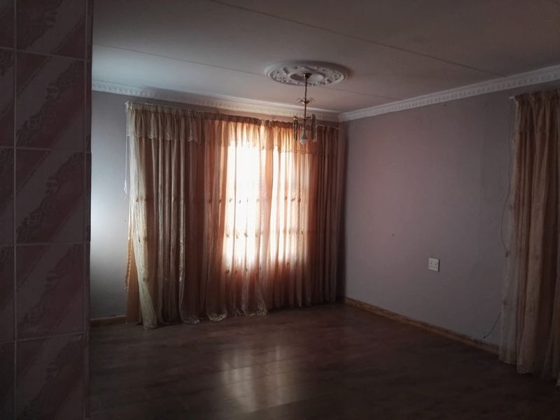 An empty living room featuring laminate flooring, decorative ceiling rose, and coving, providing a blank canvas for interior design.