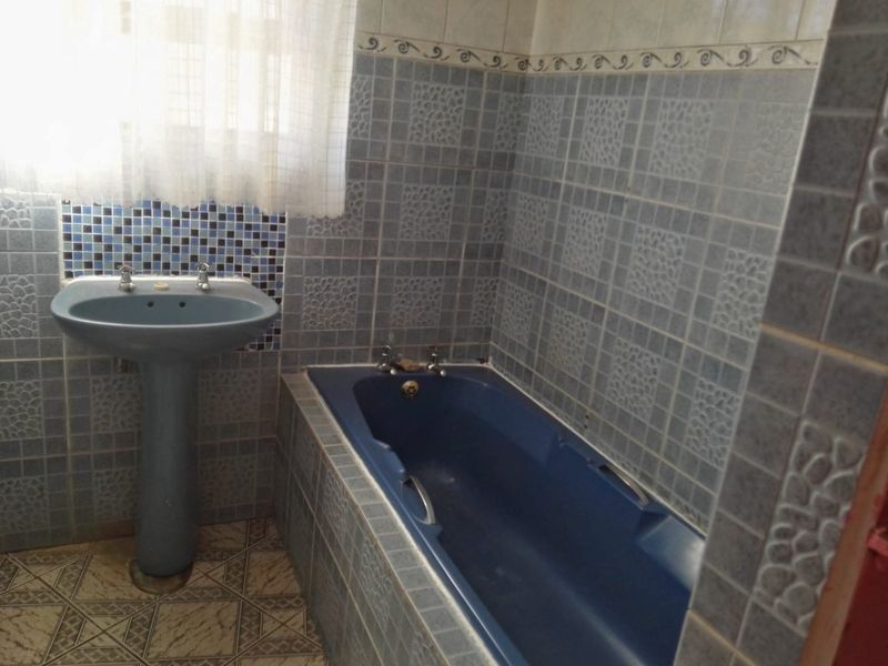A dated bathroom featuring blue sanitaryware, including a pedestal basin and a built-in bathtub, finished with patterned wall and floor tiles.