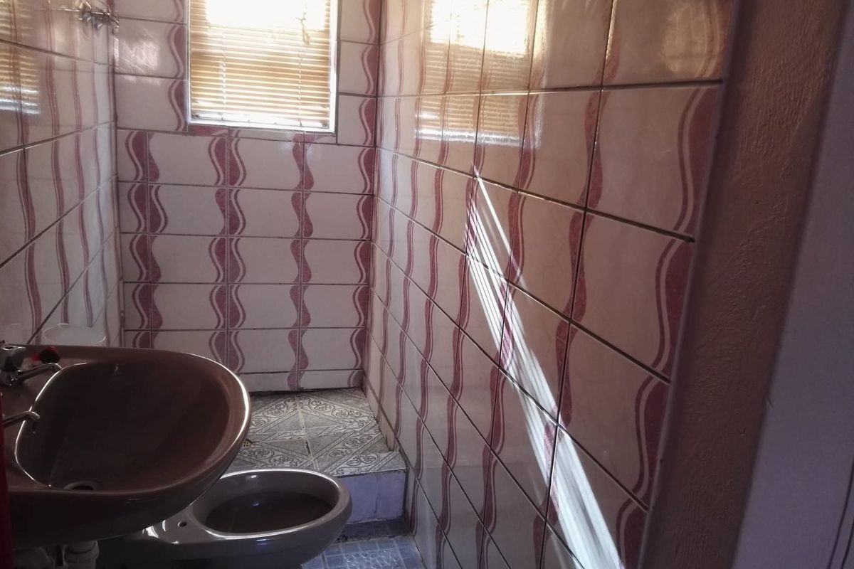A compact bathroom featuring dated wall tiling, a pedestal washbasin, and a toilet, requiring modernization to improve its aesthetic appeal and functionality.