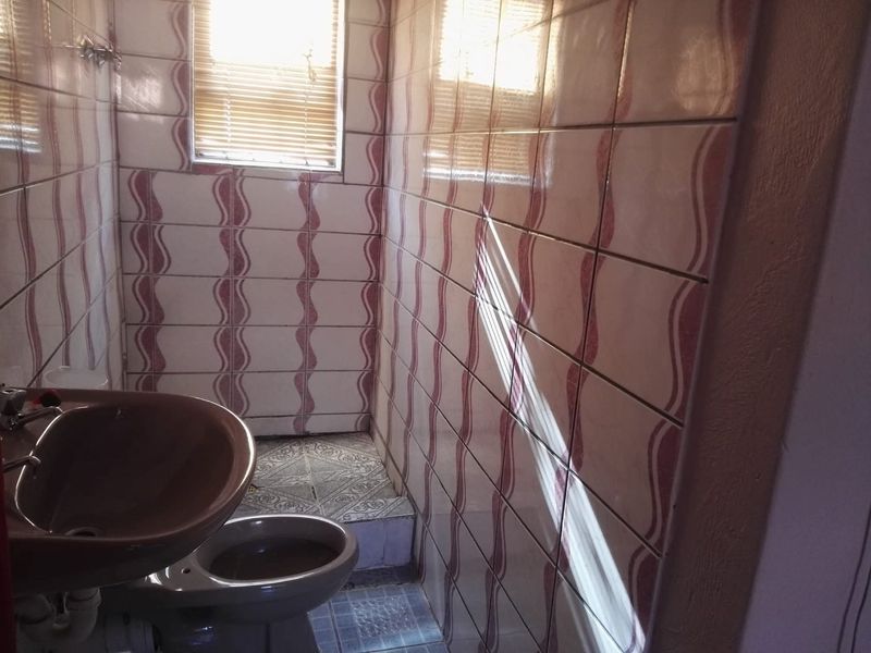 A compact bathroom featuring dated wall tiling, a pedestal washbasin, and a toilet, requiring modernization to improve its aesthetic appeal and functionality.