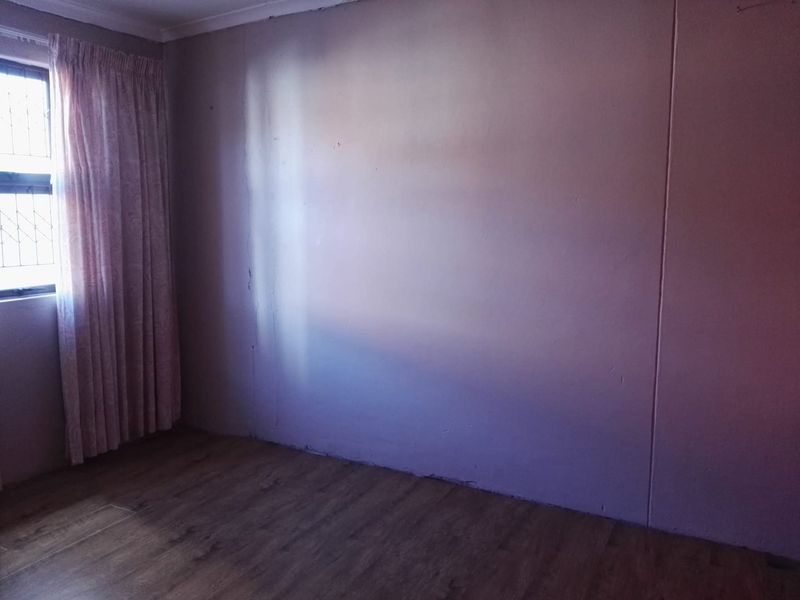An empty bedroom featuring laminate flooring and a window with security bars, requiring cosmetic updates to the wall finishes.