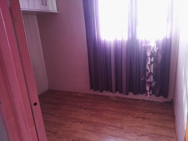 A small, empty bedroom featuring laminate flooring and built-in overhead storage cabinetry, requiring minor cosmetic updates to walls and finishes.