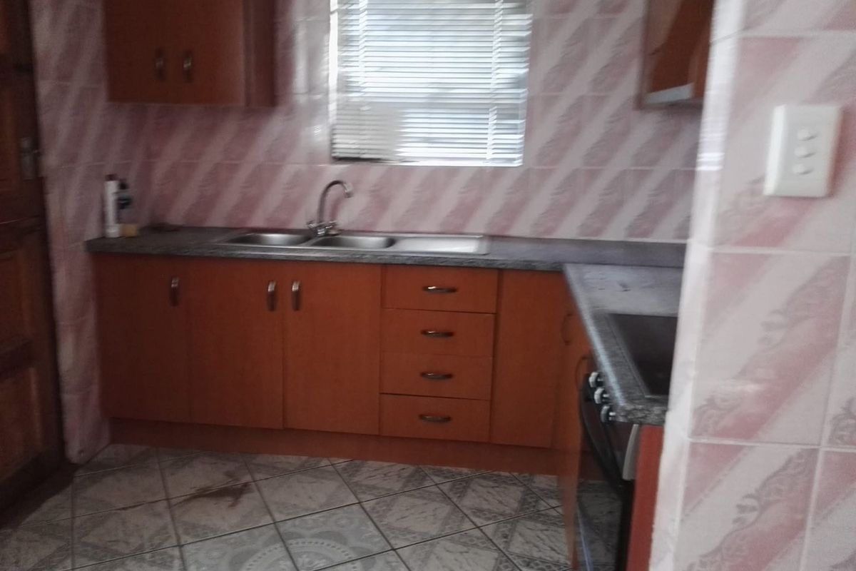 A dated kitchen featuring laminate cabinetry, a double bowl sink, and tiled finishes. The space offers functional storage and preparation areas.