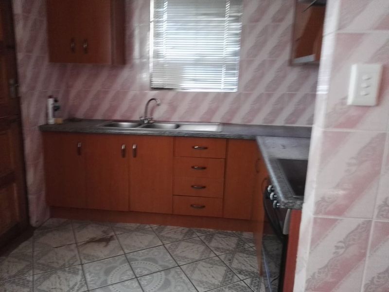 A dated kitchen featuring laminate cabinetry, a double bowl sink, and tiled finishes. The space offers functional storage and preparation areas.
