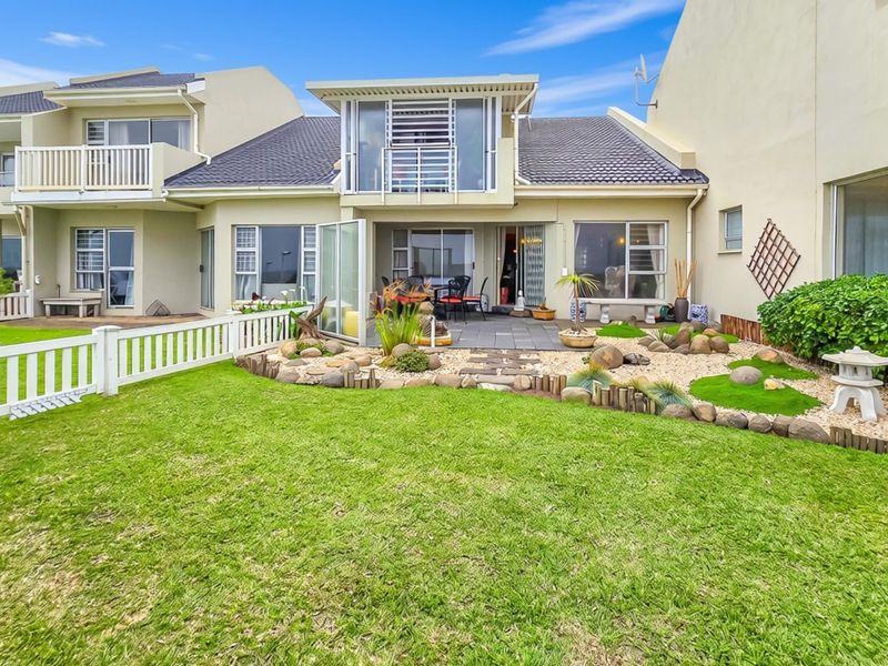 Rear view of a townhouse featuring a private garden, paved patio area, white picket fencing, and an upper-level balcony with sliding glass doors.