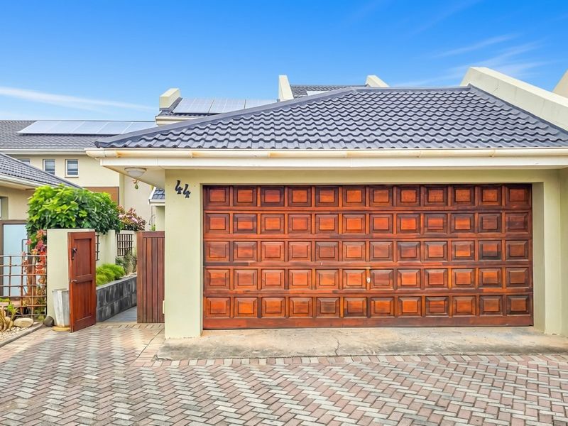 Front exterior view of a townhouse featuring a wooden garage door, paved driveway, and solar panels installed on the tiled roof.