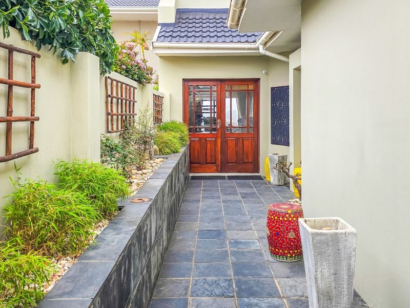 A well-maintained covered patio area featuring slate tile flooring, a raised stone planter wall, and timber double door access to the interior.