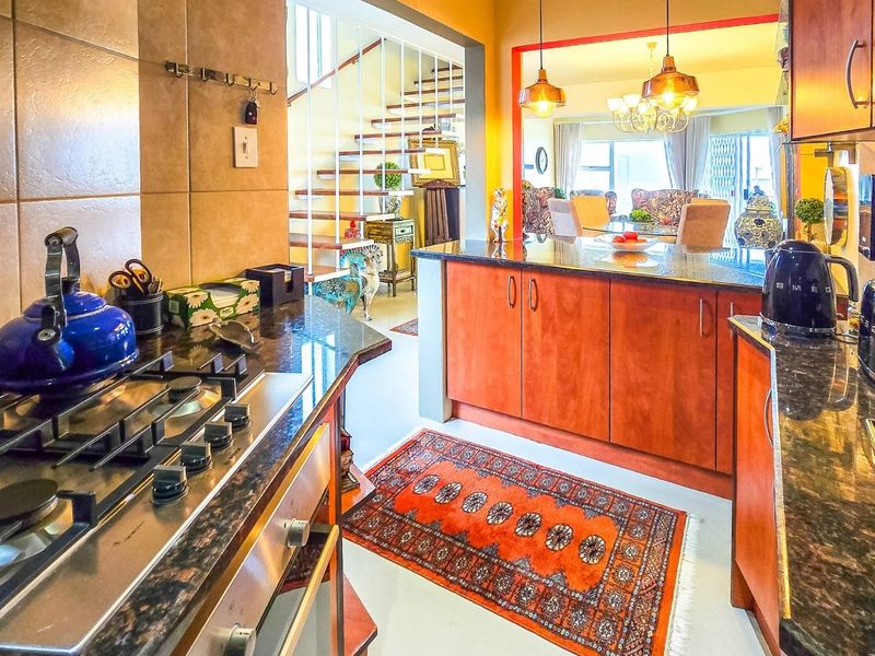 A functional kitchen featuring granite countertops, wooden cabinetry, and a gas hob, with an open-plan layout flowing into the dining and living areas.