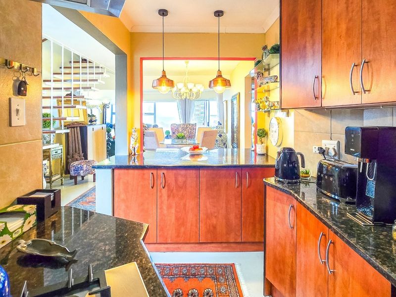 A functional kitchen featuring granite countertops, wooden cabinetry, and a tiled backsplash, with an open-plan layout leading to the dining and living areas.