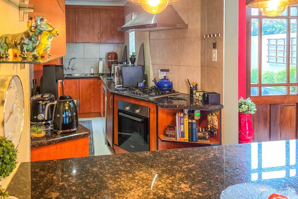 A functional kitchen featuring granite countertops, wooden cabinetry, a built-in oven, gas hob, and an extractor fan with direct access to the outdoor area.