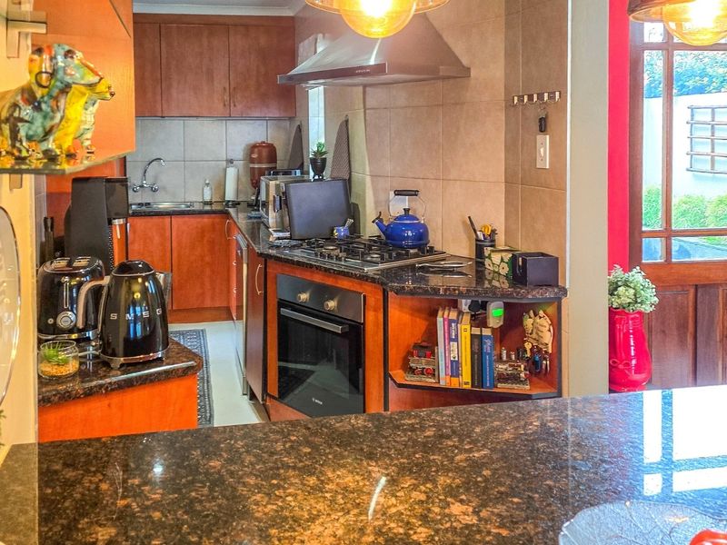A functional kitchen featuring granite countertops, wooden cabinetry, a built-in oven, gas hob, and an extractor fan with direct access to the outdoor area.