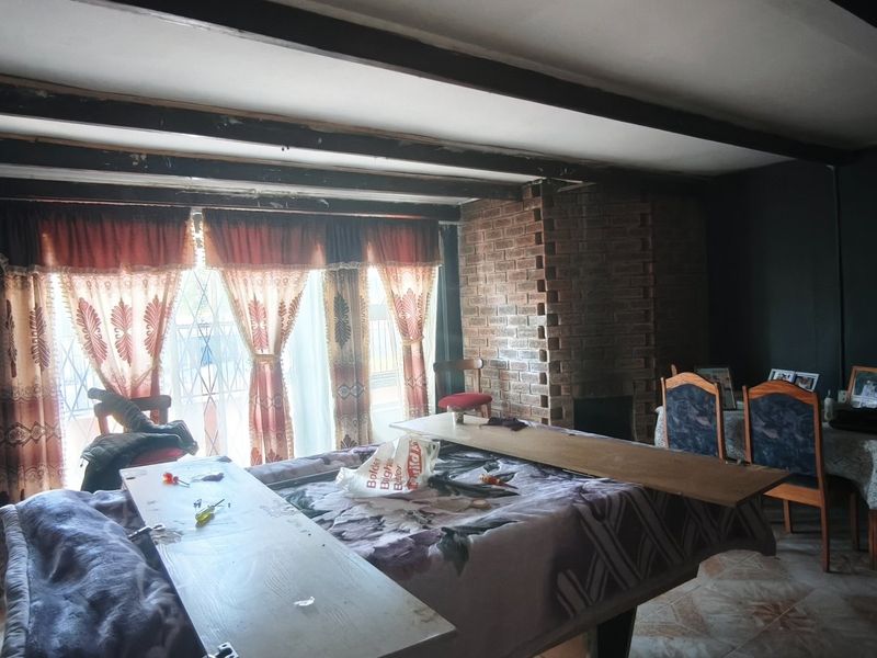 Living room featuring exposed ceiling beams, a brick fireplace, and tiled flooring, offering a rustic foundation with potential for modernization.