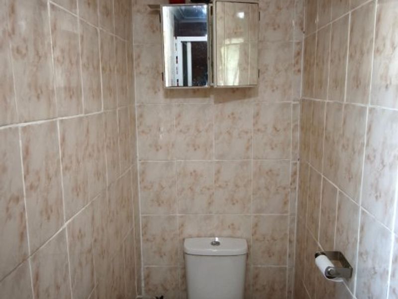 A compact guest bathroom featuring floor-to-ceiling ceramic tiling, a standard toilet, and a wall-mounted medicine cabinet.