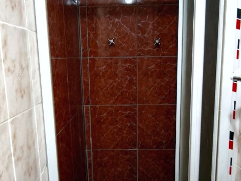 A compact shower stall featuring dated red marble-effect wall tiles and a white framed enclosure.