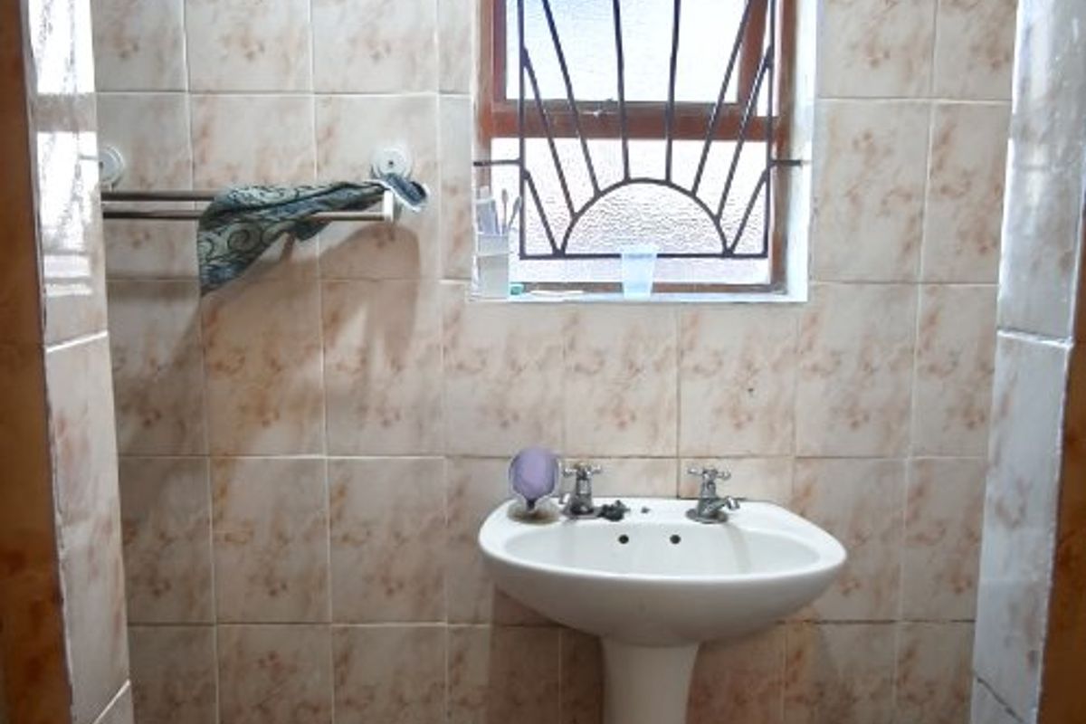 A compact bathroom featuring a pedestal basin, tiled walls and flooring, and a window with security burglar bars.