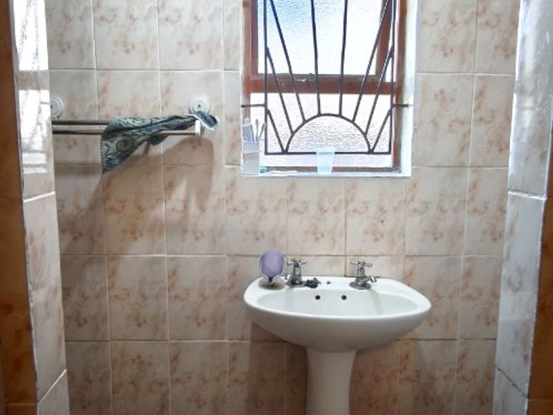A compact bathroom featuring a pedestal basin, tiled walls and flooring, and a window with security burglar bars.