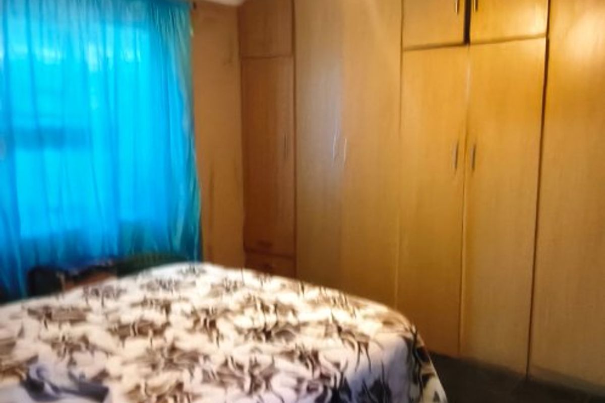 A bedroom featuring built-in wooden cupboards and dark tiled flooring, offering a functional space with potential for cosmetic updates.