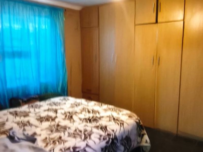 A bedroom featuring built-in wooden cupboards and dark tiled flooring, offering a functional space with potential for cosmetic updates.