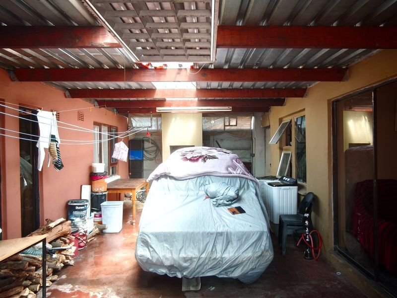 Covered patio area featuring exposed timber beams, corrugated metal roofing with a central skylight, and sliding glass door access to the main house.