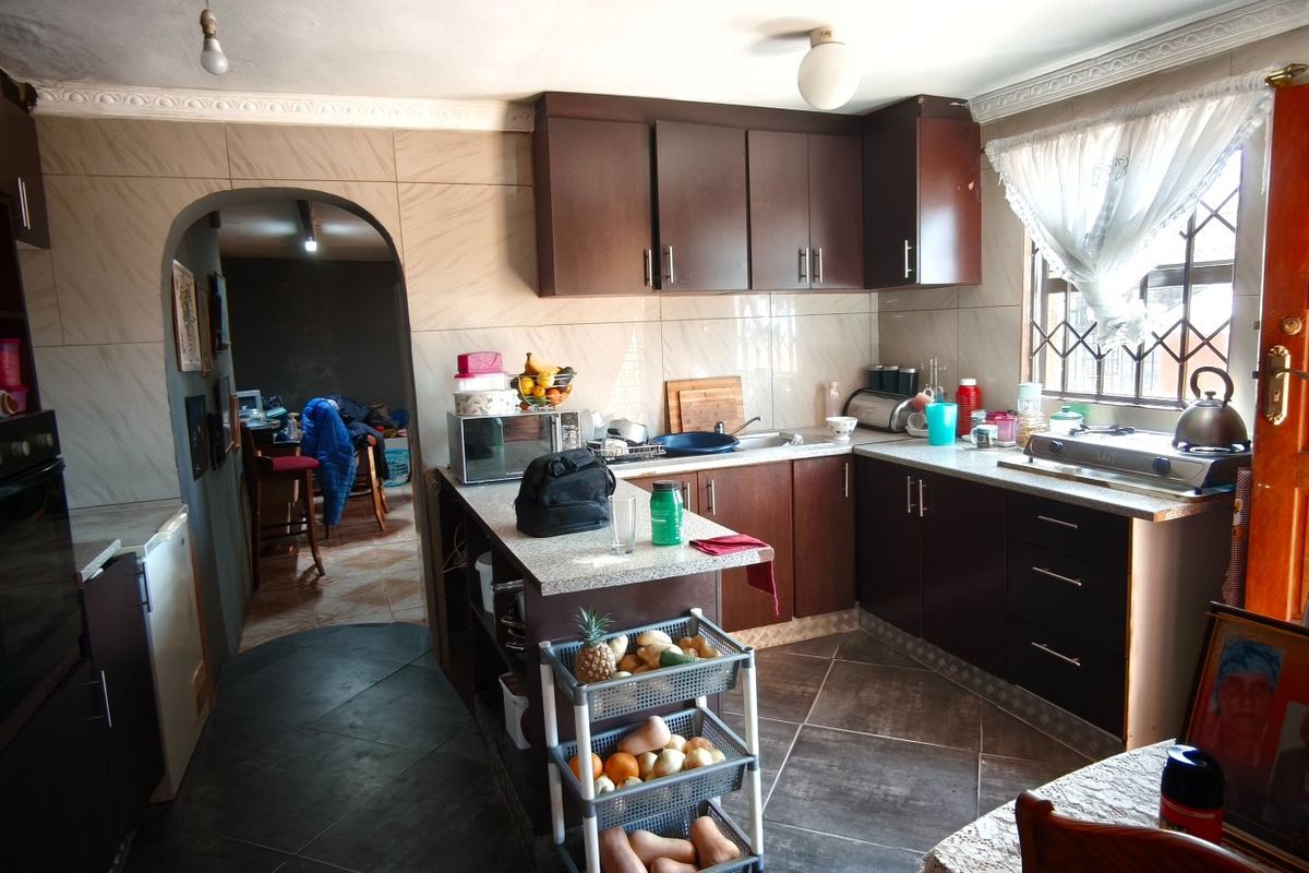 A functional kitchen featuring dark wood cabinetry, laminate countertops, built-in oven, and tiled finishes, offering a practical layout with potential for modern updates.