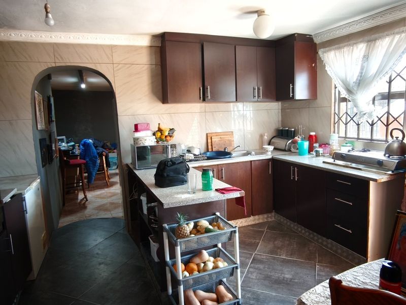 A functional kitchen featuring dark wood cabinetry, laminate countertops, built-in oven, and tiled finishes, offering a practical layout with potential for modern updates.