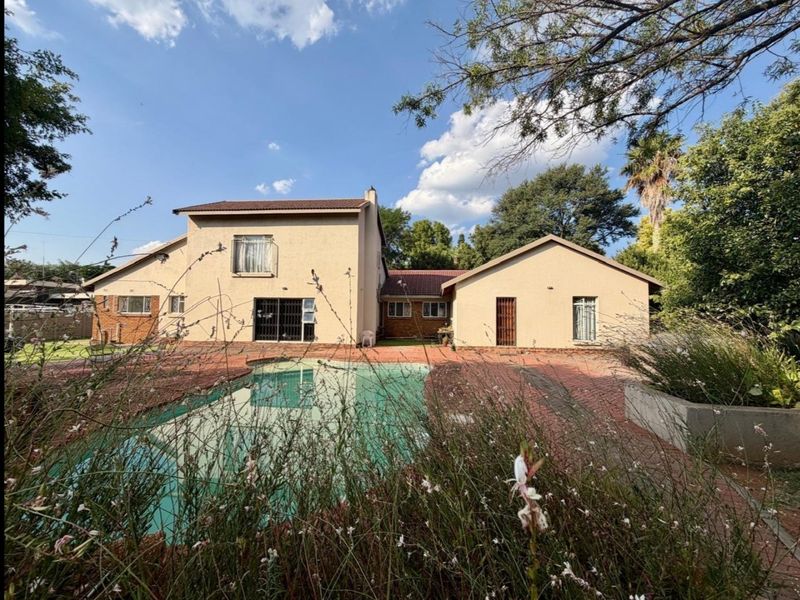 Rear view of the house featuring a swimming pool, brick paved patio area, and established garden surroundings.