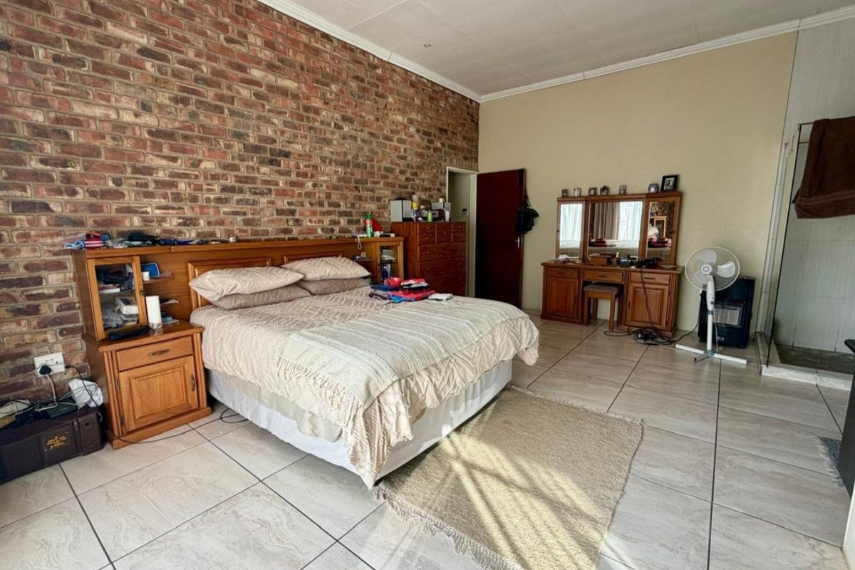 Spacious bedroom featuring an exposed brick feature wall, neutral tiled flooring, and a coved ceiling, offering a solid foundation for modern interior updates.