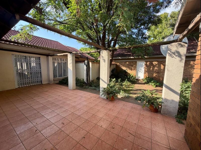 A covered outdoor patio area featuring tiled flooring, concrete support pillars, and a timber pergola, overlooking a private garden space.