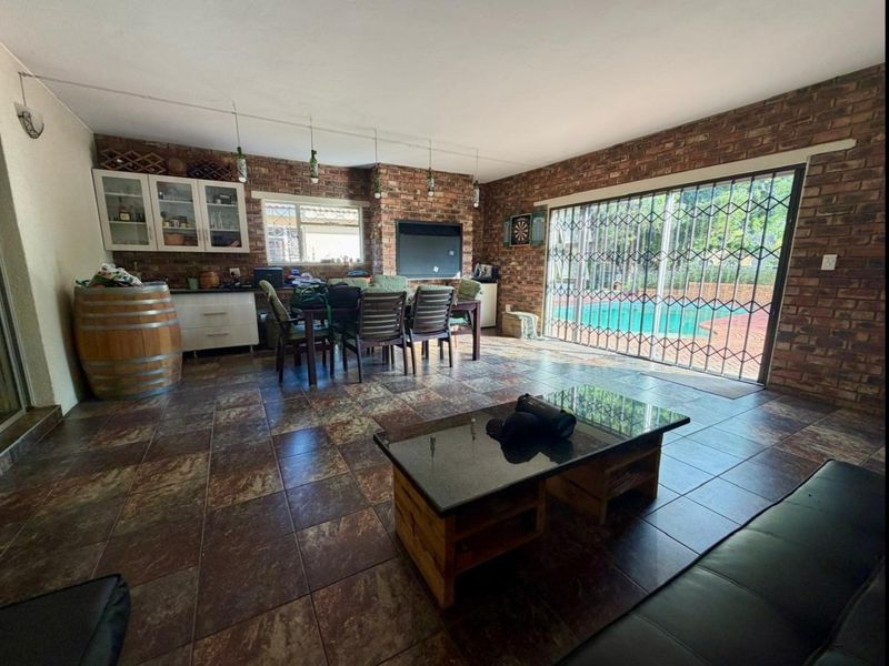 Spacious open-plan living area featuring exposed brick walls, tiled flooring, and large sliding doors providing direct access to the pool area.