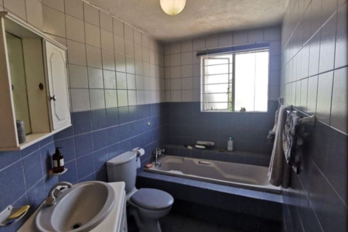 A dated bathroom featuring a built-in bathtub, wall-mounted vanity, and blue and white ceramic wall tiling throughout.
